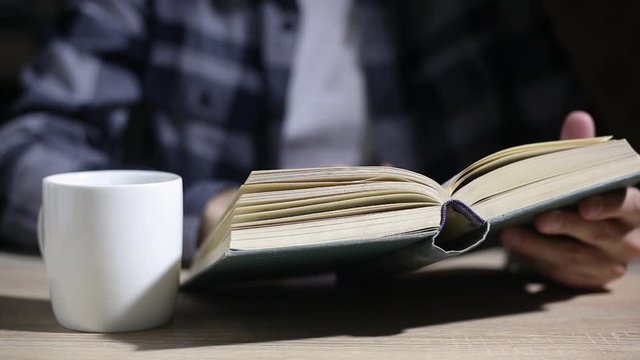 Man is reading a book, close up, isolated. Hand open book for reading. Man is looking for information in book. Close-up macro shot picture of hand and book isolated on black background