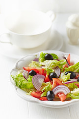 Healthy salad with black olives, tomatoes and red onion on bright wooden background.