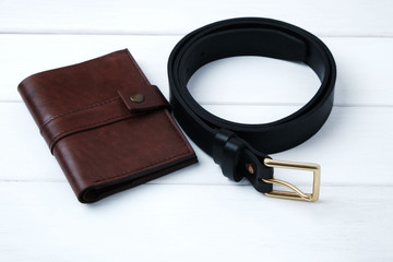 Wallet and belt made of genuine leather on white wooden background with copy space