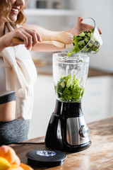 cropped view of woman holding bowl with fresh lettuce and cucumber near blender