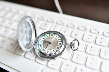 Antique vintage pocket watch lies on white keyboard. The concept of modernity, manufacturability,...