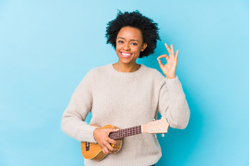 Young african american woman playing ukelele isolated cheerful and confident showing ok gesture.