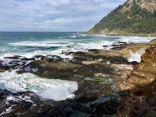 The Oregon coast with ocean waves crashing against the sand, and mountains in the background. 