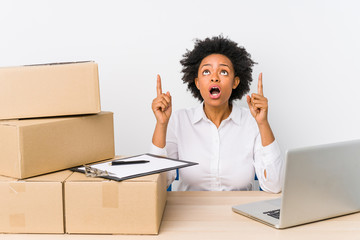 Warehouse manager sitting checking deliveries with laptop pointing upside with opened mouth.