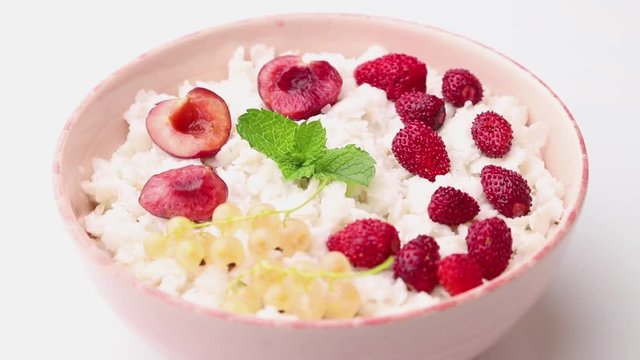 Rotating of rice flakes porridge with milk and strawberry in ceramic bowl on white background. Side view, close up.