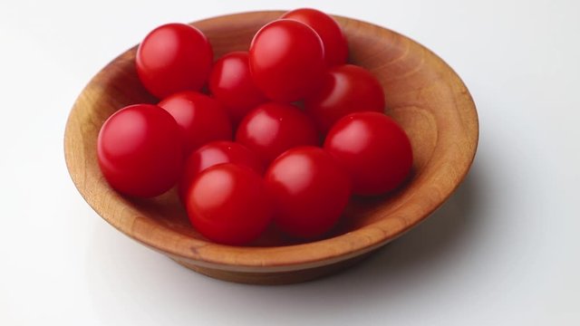 Rotating of cherry tomatoes in wooden plate on white background. Side view, close up.