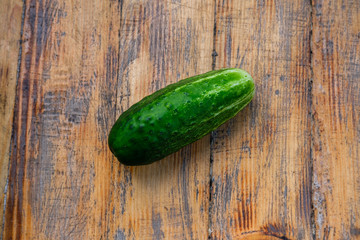 A large overgrown green cucumber lies on a shabby wooden table.