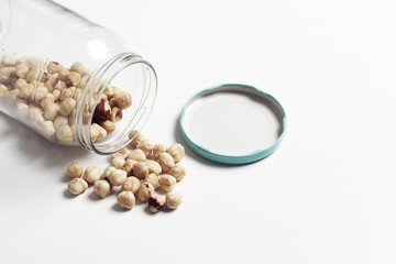 chickpeas spilling from a glass jar on white background.