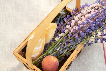 Romantic picnic for a couple. Basket with flowers, wine, peaches and baguettes on a background of bright summer grass, top view