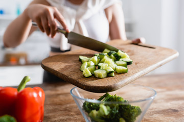 cropped view of woman holding cutting board with sliced cucumber near bowl with broccoli