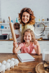 selective focus of girl holding rolling pin and sieve near mother with infant son