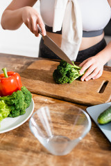 cropped view of woman cutting fresh broccoli on chopping board near vegetables