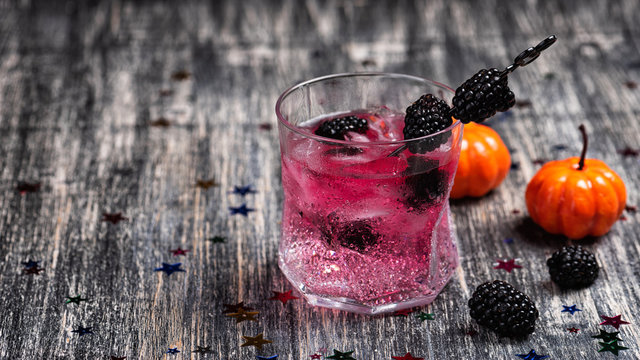 Sparkling alcoholic cocktail with a blackberry and basil on wooden table with glitter stars. Detox water and halloween pumpkin