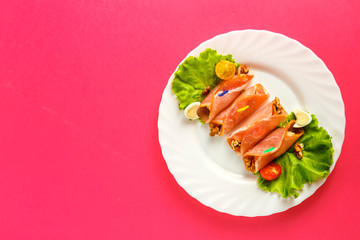 rolls with ham on a plate with green salad on a pink background. save a place