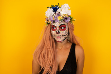 Oops! Portrait of female wearing halloween make up with specific appearance clenches teeth and looks confusedly aside, realizes her bad mistake, poses against copy area for your advertising.