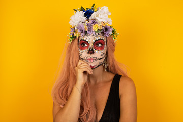 Portrait of thoughtful  woman wearing halloween make up keeps hand under chin, looks away trying to remember something or listens something with interest, dressed casually. Youth concept.