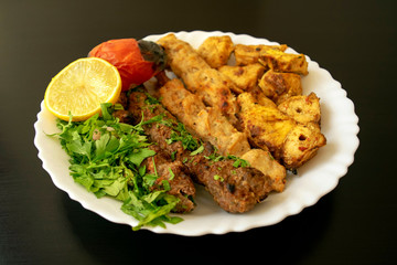Famous traditional Arabic, Turkish, Israel food. Grilled chicken shashlik, lamb, beef kofta kebab, vegetables, lemon on white plate on dark wooden background, close up. Kafta kebab