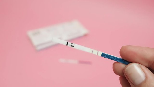 Female hand holding positive pregnancy test isolated on pink background. The abbreviation HCG on the blue bar means Human chorionic gonadotropin is a hormone produced by cells that are surrounding a