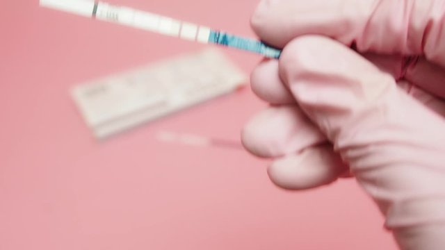Female hand in a pink medical glove holding positive pregnancy test isolated on pink background. The abbreviation HCG on the blue bar means Human chorionic gonadotropin is a hormone produced by cells