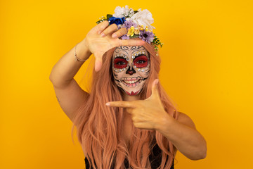 Portrait of young blonde positive female with cheerful expression, dressed in casual light blue sweater, has good mood, gestures finger frame actively at camera.
