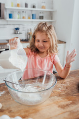 little girl pouring flour into glass bowl while cooking in kitchen