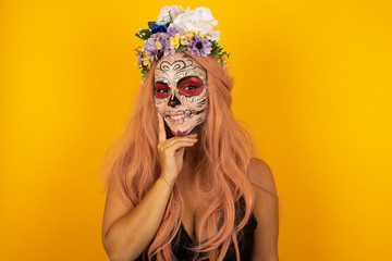 Carefree successful female wearing sugar skull Halloween make up smiling broadly self-assured touching jawline gazing camera tilting head grinning white teeth delighted