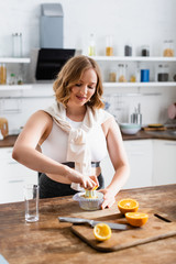 selective focus of young woman squeezing orange while preparing juice in kitchen