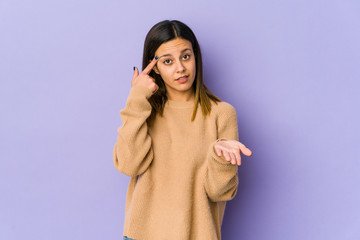 Young woman isolated on purple background holding and showing a product on hand.