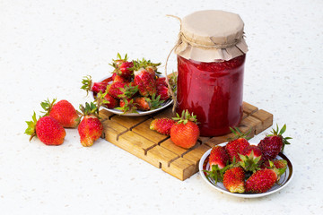 Strawberry berries on a white plate on a cutting Board with a jar of strawberry jam on a light background with cookies. Flatly. The view from the top.