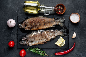 Fried fish trout with spices and ingredients on stone background