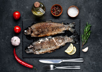 Fried fish trout with spices and ingredients on stone background