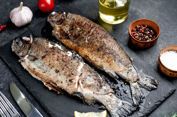 Fried fish trout with spices and ingredients on stone background