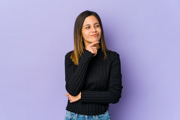 Young woman isolated on purple background thinking and looking up, being reflective, contemplating, having a fantasy.