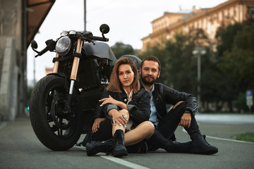 Fototapeta na wymiar Beautiful biker couple in love are sitting on the road next to motorcycles in the city