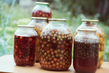 Jars with kompot on table. Sealed glass jars with kompot placed on table near flowers and fruits on summer day in garden