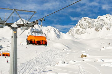 Ski lift ropeway on hilghland alpine mountain winter resort on bright sunny day. Ski chairlift cable way with people enjoy skiing and snowboarding.Banner panoramic wide view of downhill slopes