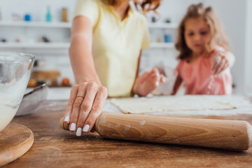 cropped view of mother taking rolling pin near daughter and dough on kitchen table, selective focus