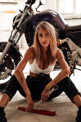 Fototapeta na wymiar Smiling sexy girl with wrenches posing with a sport motorcycle