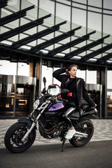 Fototapeta na wymiar Cool girl in a motorcycle jacket sits with a motorcycle helmet on a motorbike