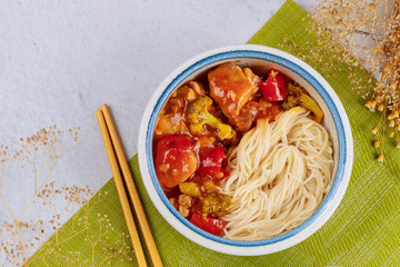 Chicken teriyaki with bell peppers, broccoli and noodles in bowl with chopsticks.