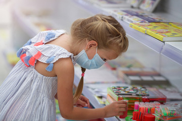 A girl in a medical mask in a shopping center buys stationery for school. Preparing for school after quarantine Covid - 19.