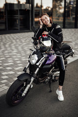 Fototapeta na wymiar Happy girl in a black jacket sits on a purple motorbike with a red safety helmet