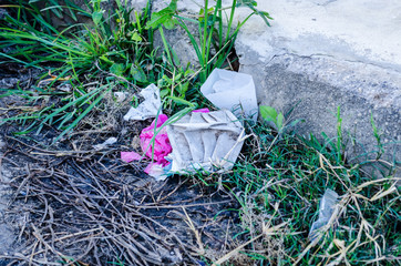 white disposable mask thrown on the street with other garbage accumulated in a curb