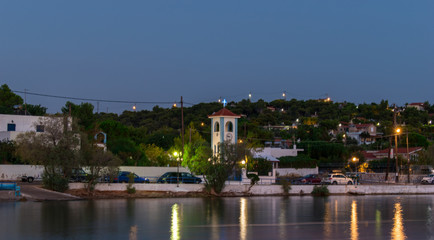Salamina, Greece - August 16, 2020: Landscape view of a coastal road in Salamina island Greece with light reflection on the sea water. Full of green trees hill view in the background..