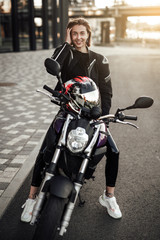 Naklejka premium Pretty smiling girl in a black jacket sits on a purple motorbike with a red safety helmet