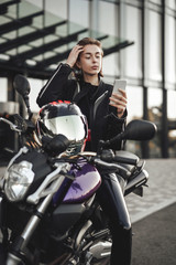 Fototapeta na wymiar Beauty in a motorcycle jacket sits on a purple motorbike and looks at her phone