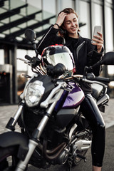 Young girl in a motorcycle jacket sits on a purple motorbike and looks at her phone