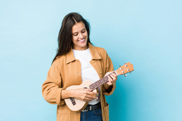 Fototapeta premium Young caucasian woman playing ukelele isolated on a blue background