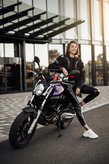 Obraz na płótnie Canvas Very happy girl in a black jacket sits on a purple motorbike with a safety helmet