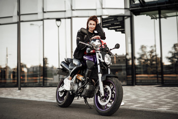 Fototapeta na wymiar Cute girl in a motorcycle jacket sits with a motorcycle helmet on a motorbike